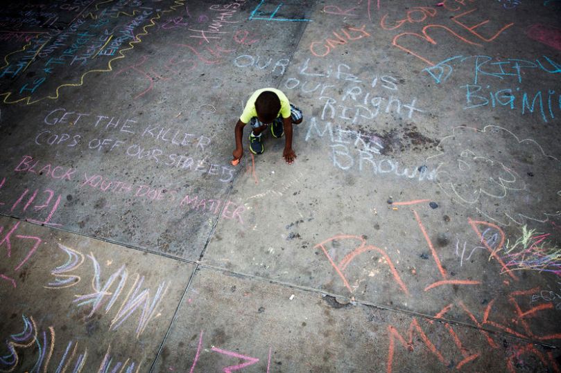 Young boy uses sidewalk chalk to draw on a parking lot filled with memorial slogans during a demonstration to protest shooting of Michael Brown and resulting police response to protests, in Ferguson, Missouri